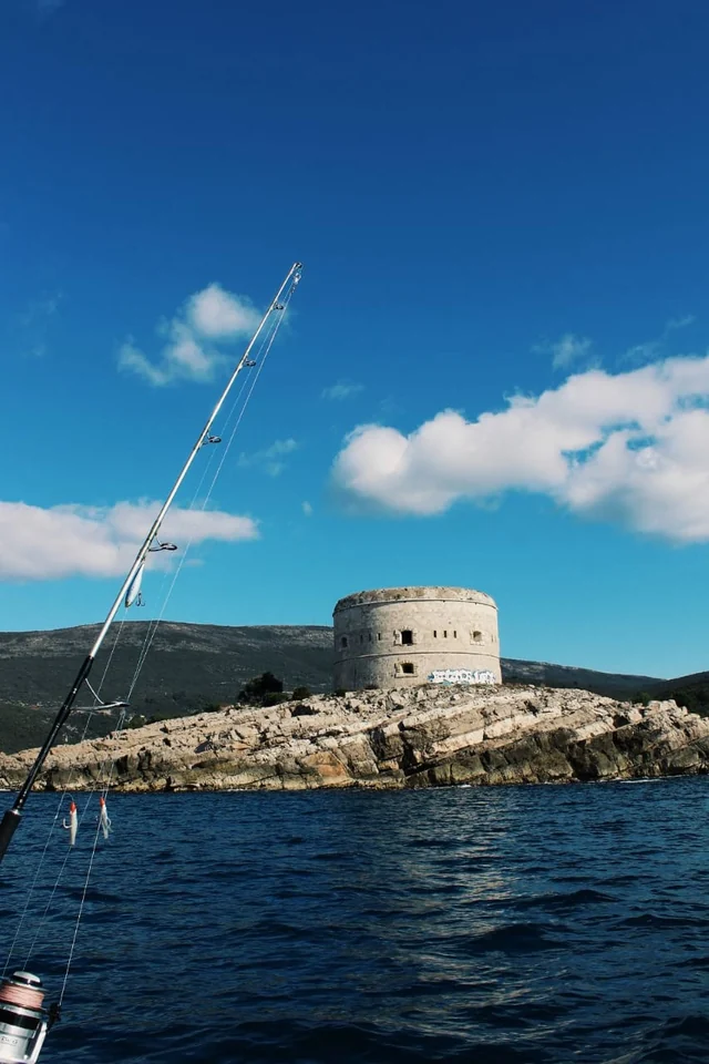 A round stone coastal fortress with a fishing rod in the foreground.