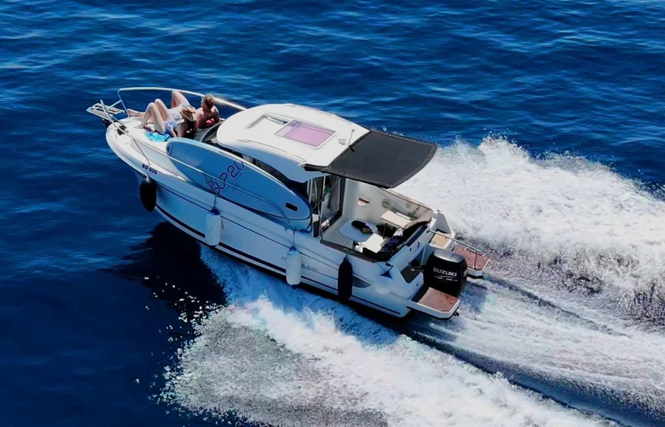 Antares 606 underway with guests on the bow, a paddleboard along the side and a foaming wake.