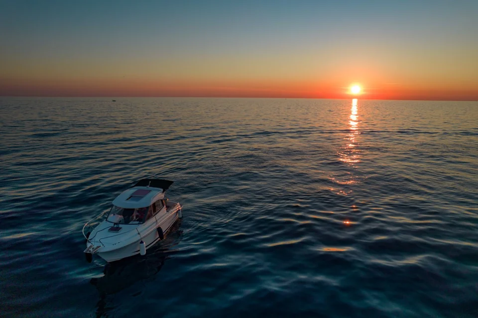 Antares 606 on calm water beneath the setting sun and its golden reflection.