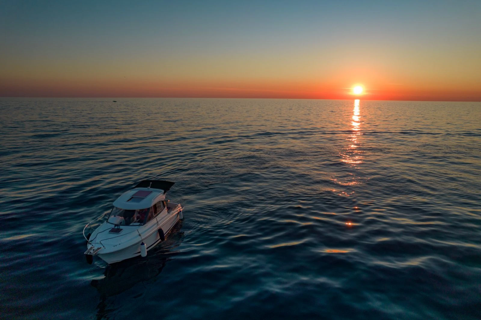 Antares 606 on calm water beneath the setting sun and its golden reflection.