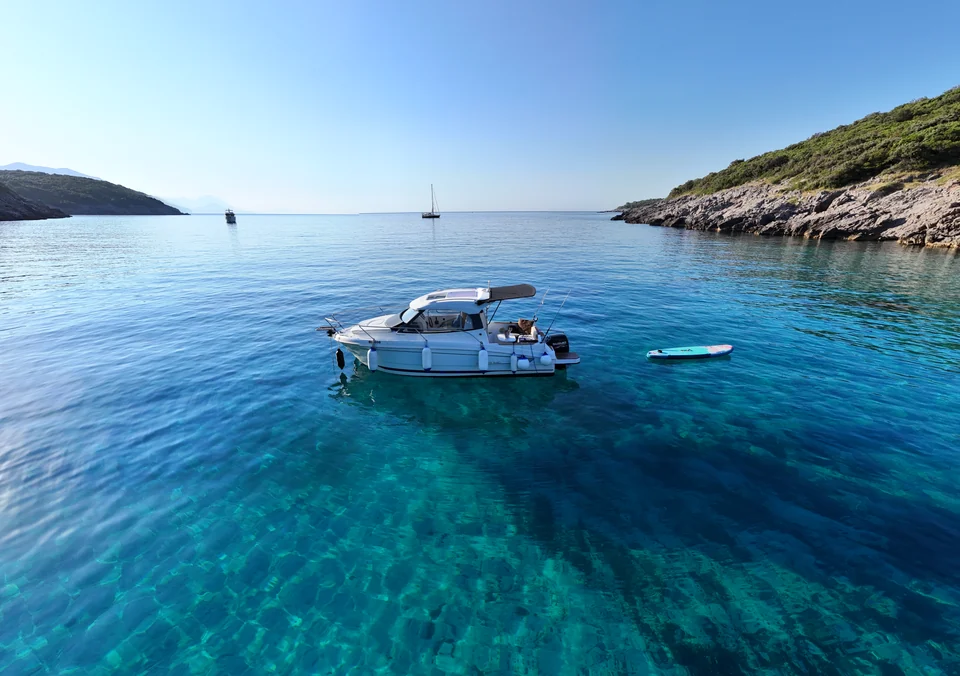 Antares 606 and a paddleboard floating in turquoise water beside a rocky coast.