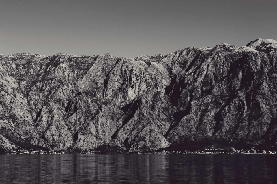 Black-and-white view of rugged mountains and the shoreline of Boka Bay.