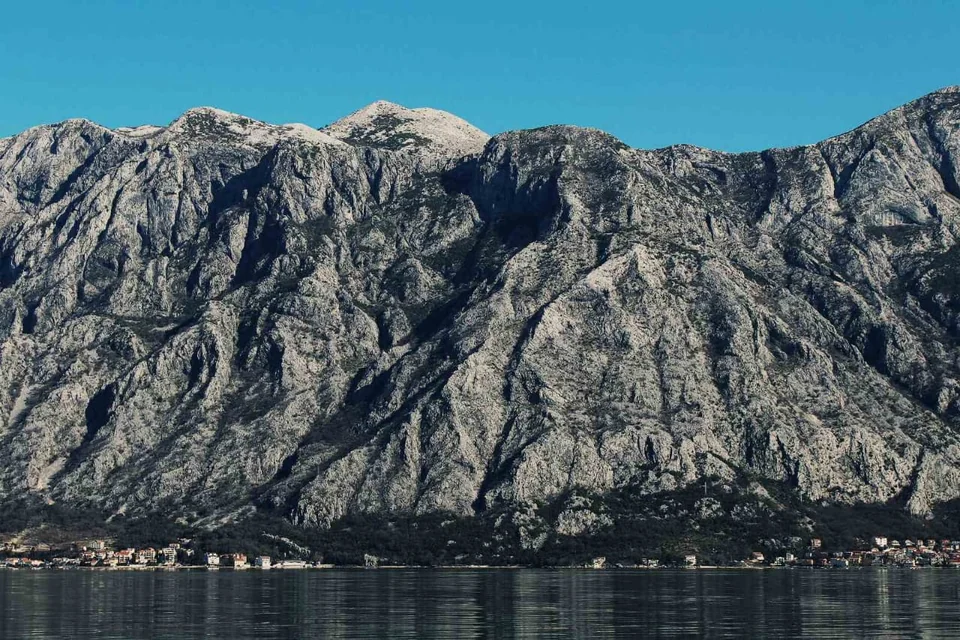 Steep rocky mountains rising above waterfront houses in Boka Bay.