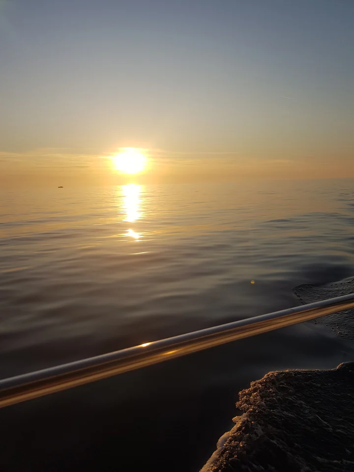 A low golden sun reflected across calm sea beside the boat's rail.
