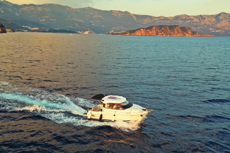 Antares 606 cruising in warm evening light with coastal cliffs and mountains behind.