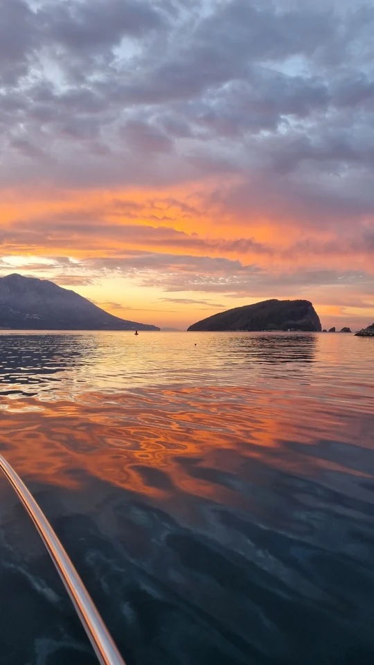 Orange clouds reflected on the sea between coastal hills.