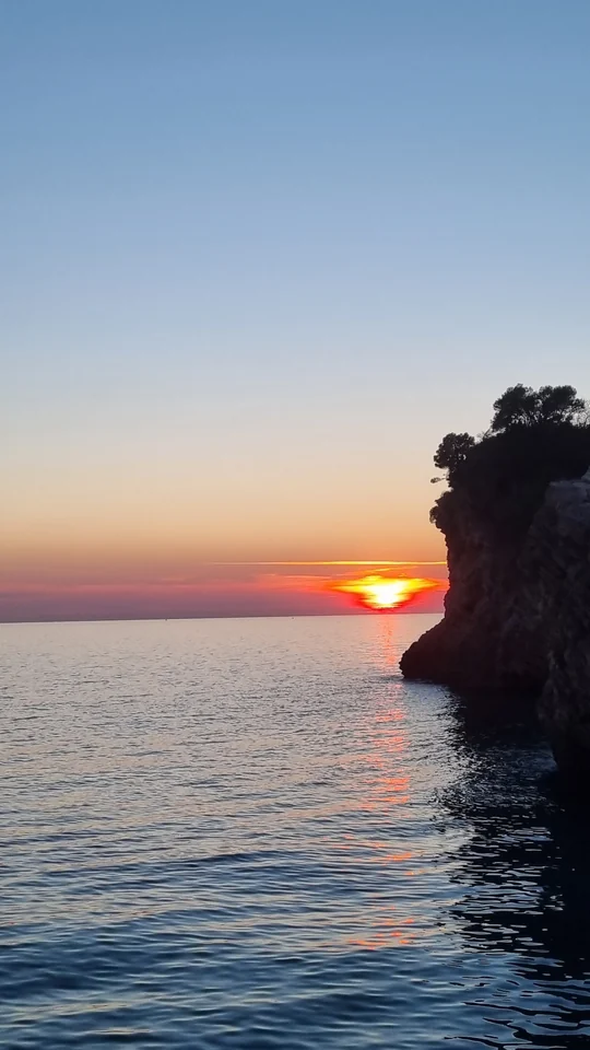 Sunset over the sea beside a steep rocky cliff.
