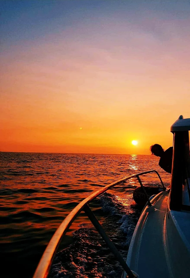 Orange sunset over the sea beside the boat's deck and curved rail.