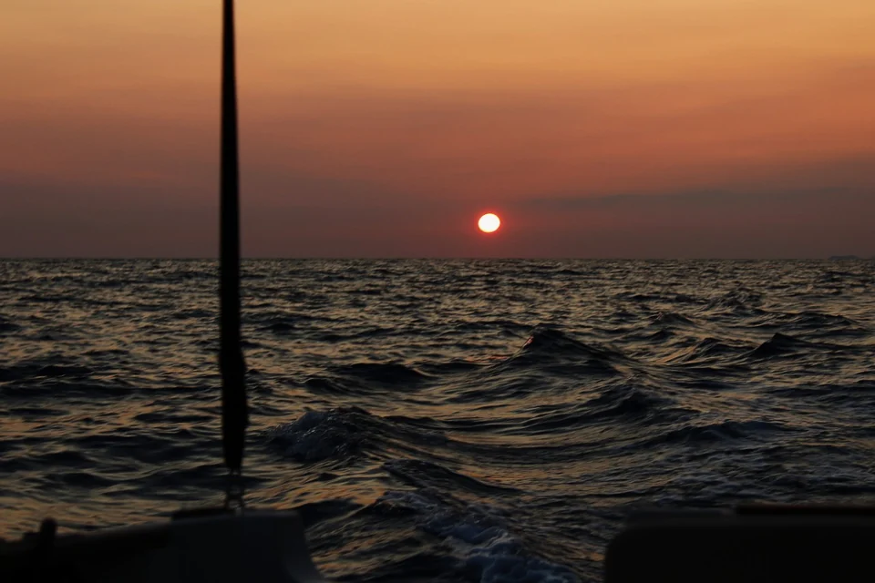 The setting sun above open water, framed by a fishing rod on the boat.