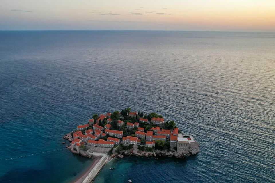 Aerial view of Sveti Stefan's stone buildings, red roofs and causeway beside the sea.